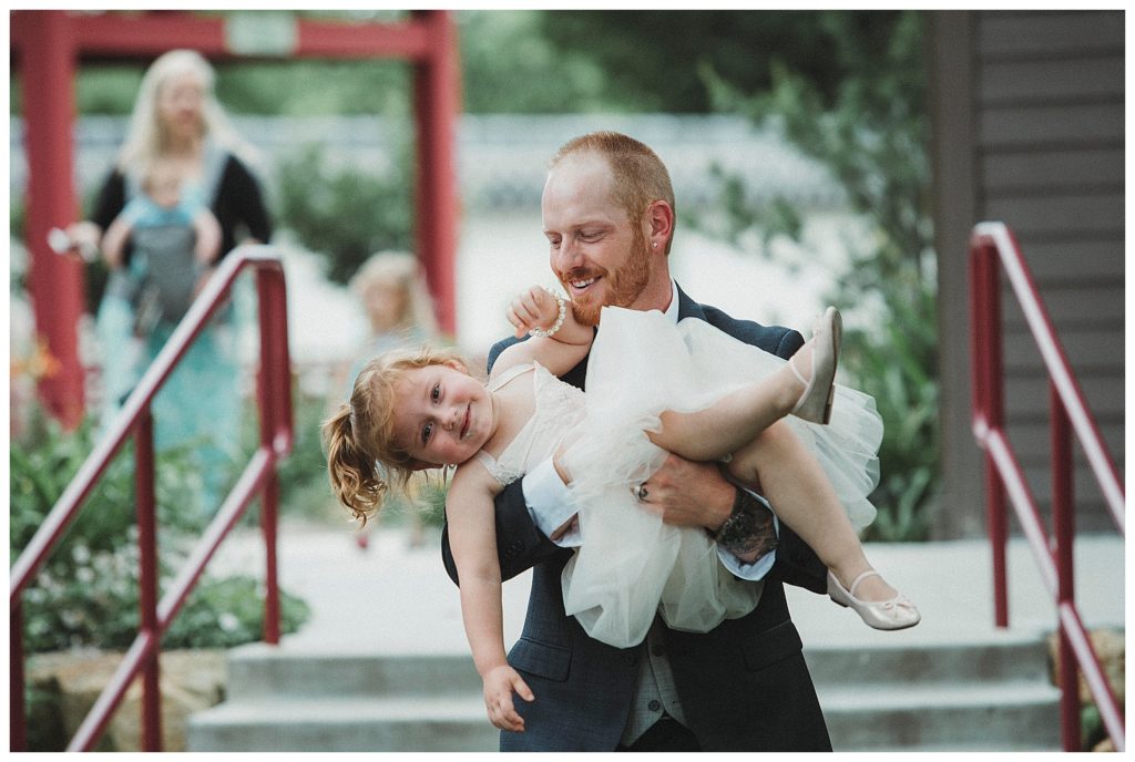 groom carrying the flower girl