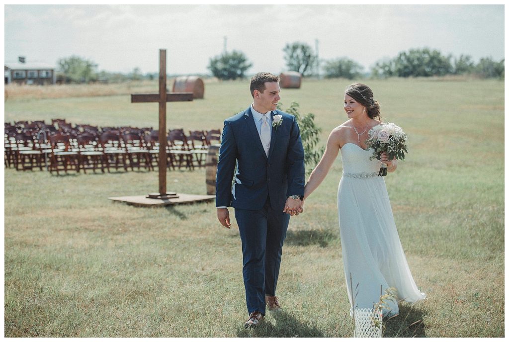 bride and groom walking with cross in background