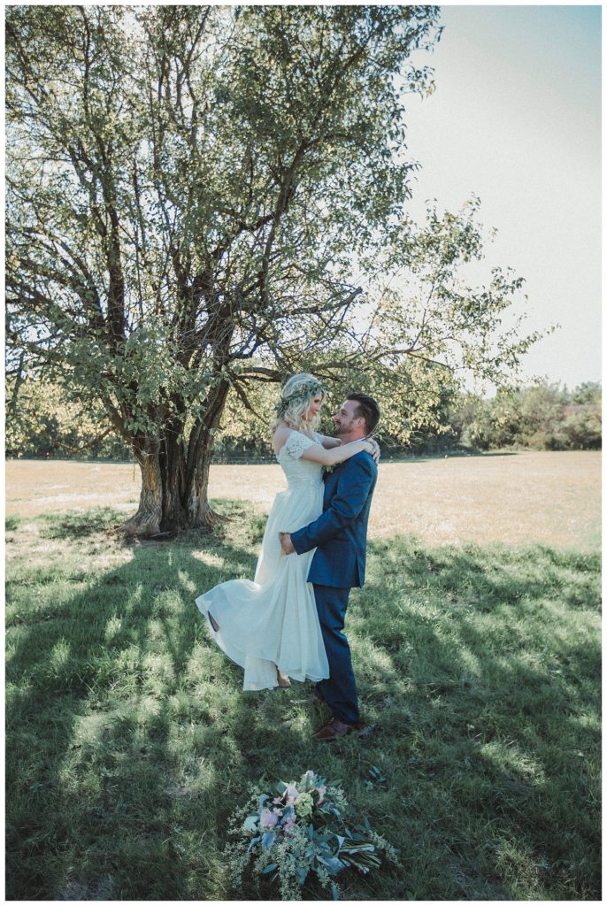 groom picking up bride in front of large tree