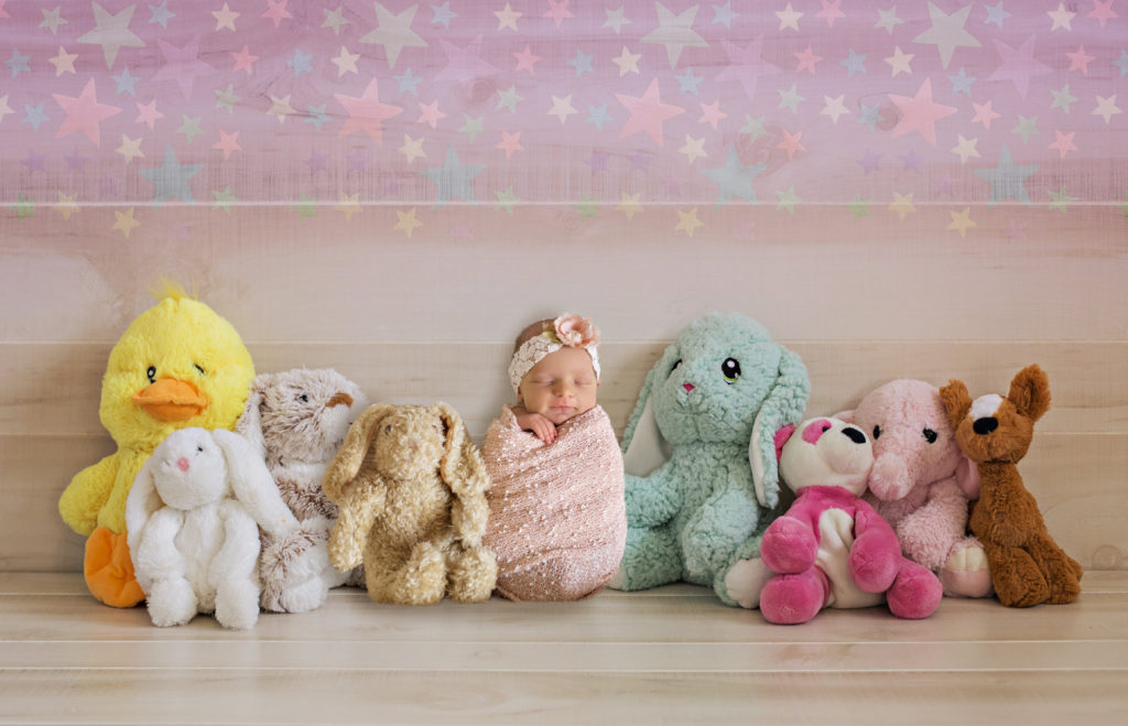 newborn girl sitting next to stuffed animals