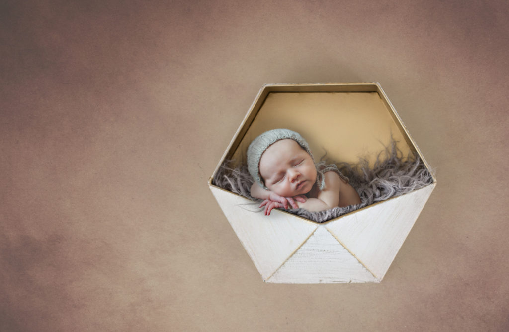newborn boy with bonnet nestled in tin
